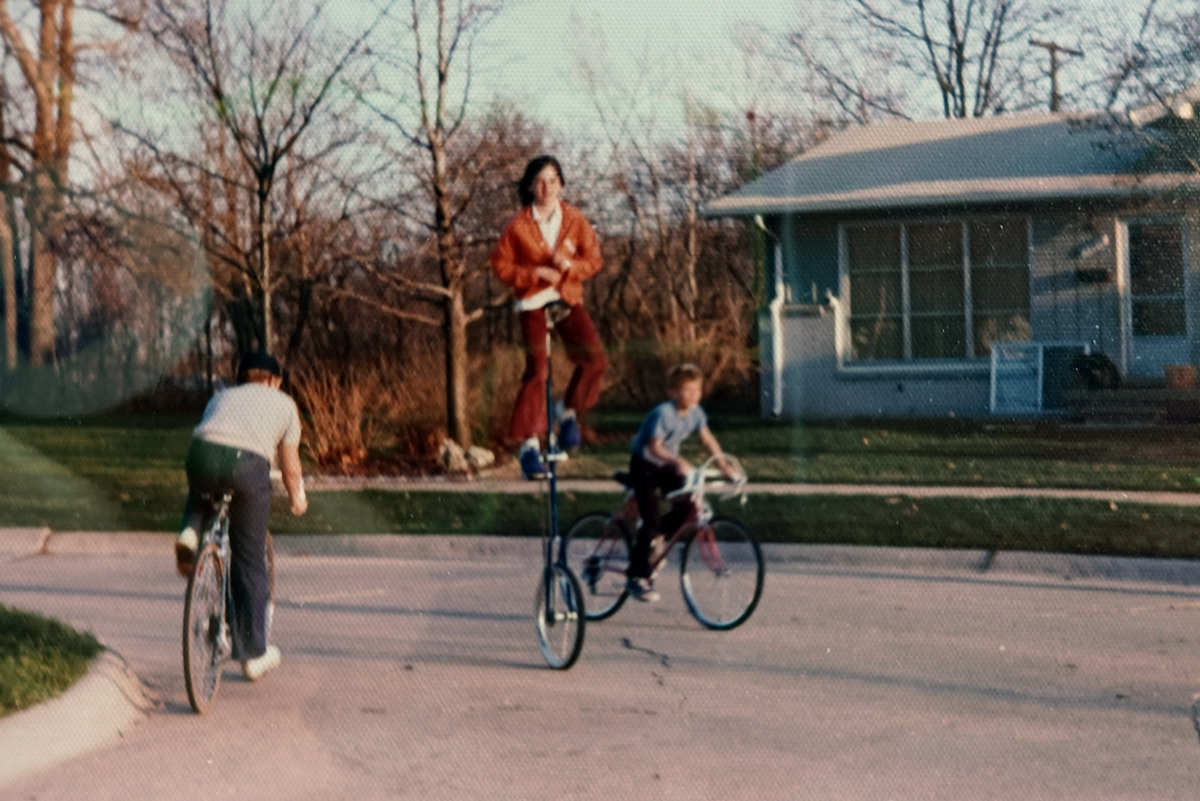 One kid riding a tall unicycle and two kids riding bicycles.