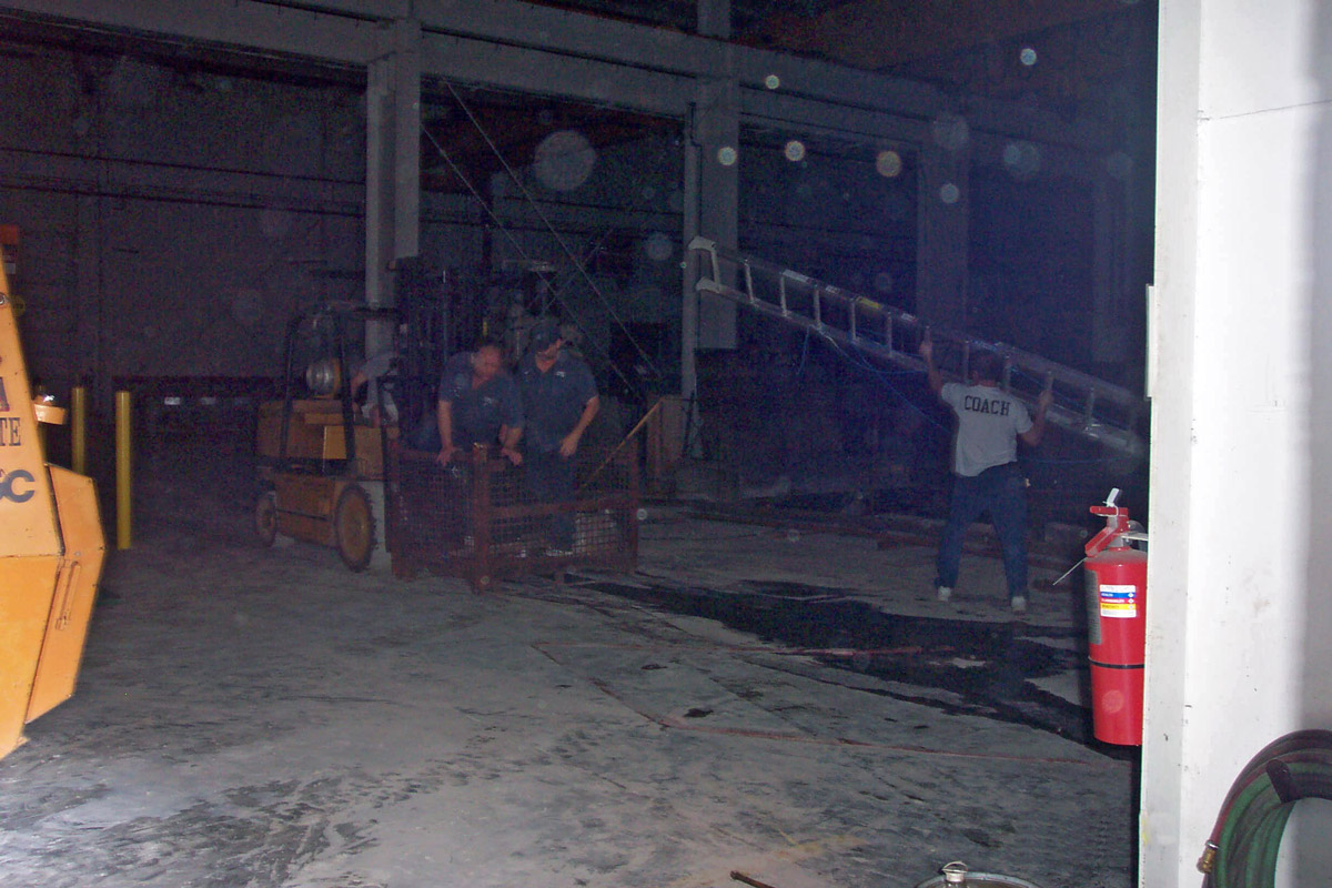 Two guys standing in a parts basket and a guy holding a ladder.
